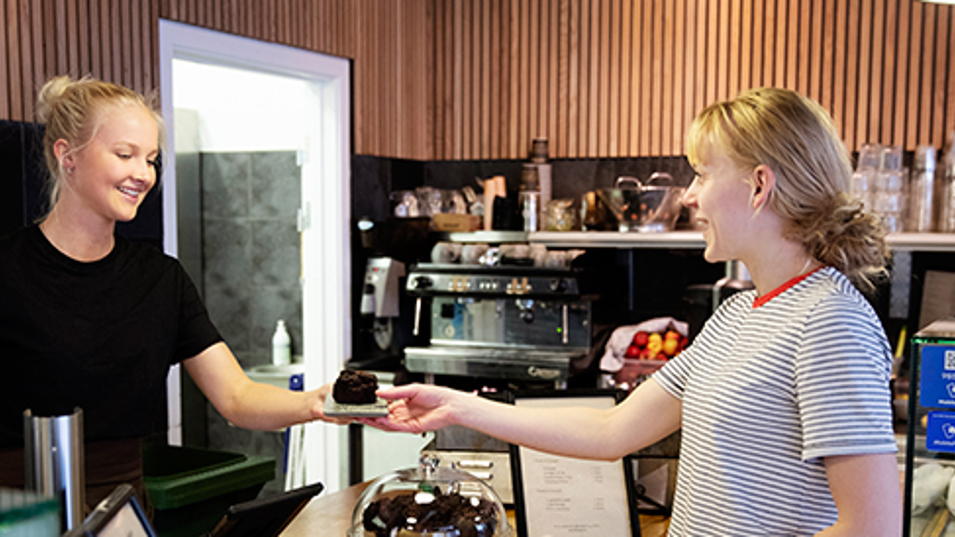 En kafemedarbejder der giver ud kage til en gæst