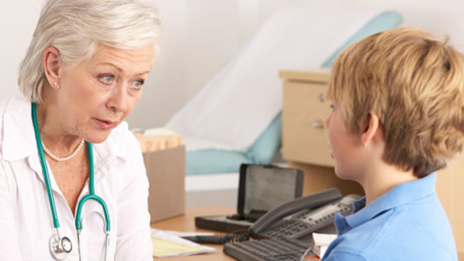 En ældre kvindelig læge der taler med en dreng