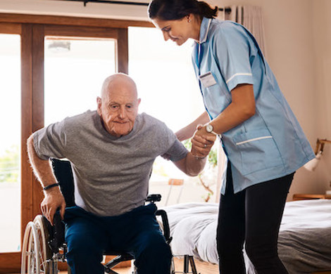 A healthcare assistant helping an elderly resident rise from a wheelchair.