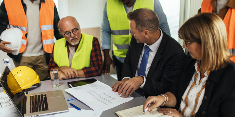 Leder snakker med medarbejdere i en skurvogn på en byggeplads.