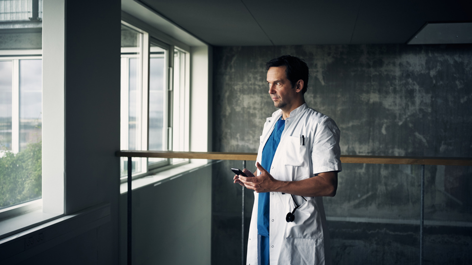 En hospitalsmedarbejder står med sin smartphone i hånden