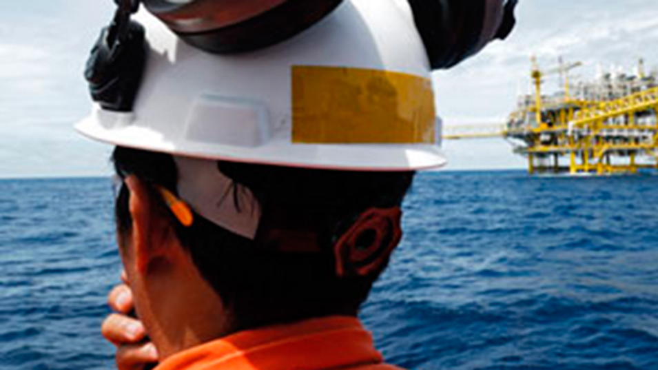 En der har arbejdstøj og sikkerhedshjelm på, som kigger ud mod en oljeplatform