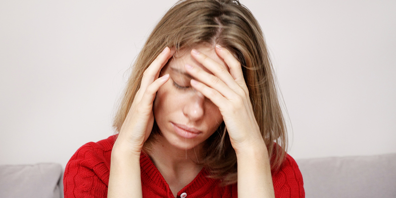 En ung kvinde sidder ved et bord og tager sig til hovedet.