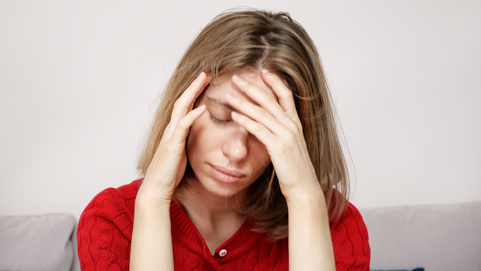 En ung kvinde sidder ved et bord og tager sig til hovedet.