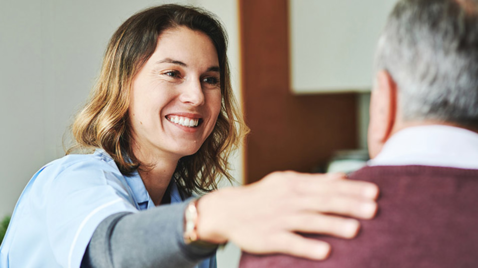 A healthcare assistant smiling while helping and listening to an elderly resident.