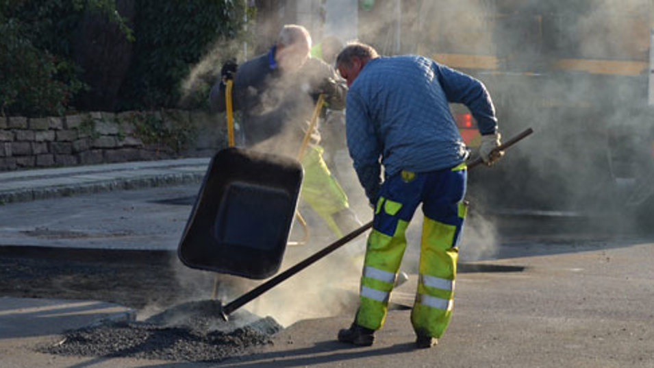 To personer der sammen reparerer huller i asfalten på en vej