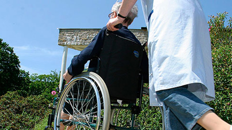 En sosu-assistent kører en mand i en rullestol udenfor i en smuk have