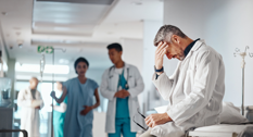 En læge der sidder på en hospitalsgang og tager sig til hovedet
