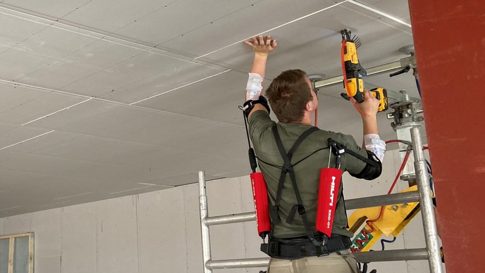 Tømrer iført skulder-exoskelet under loftmontering